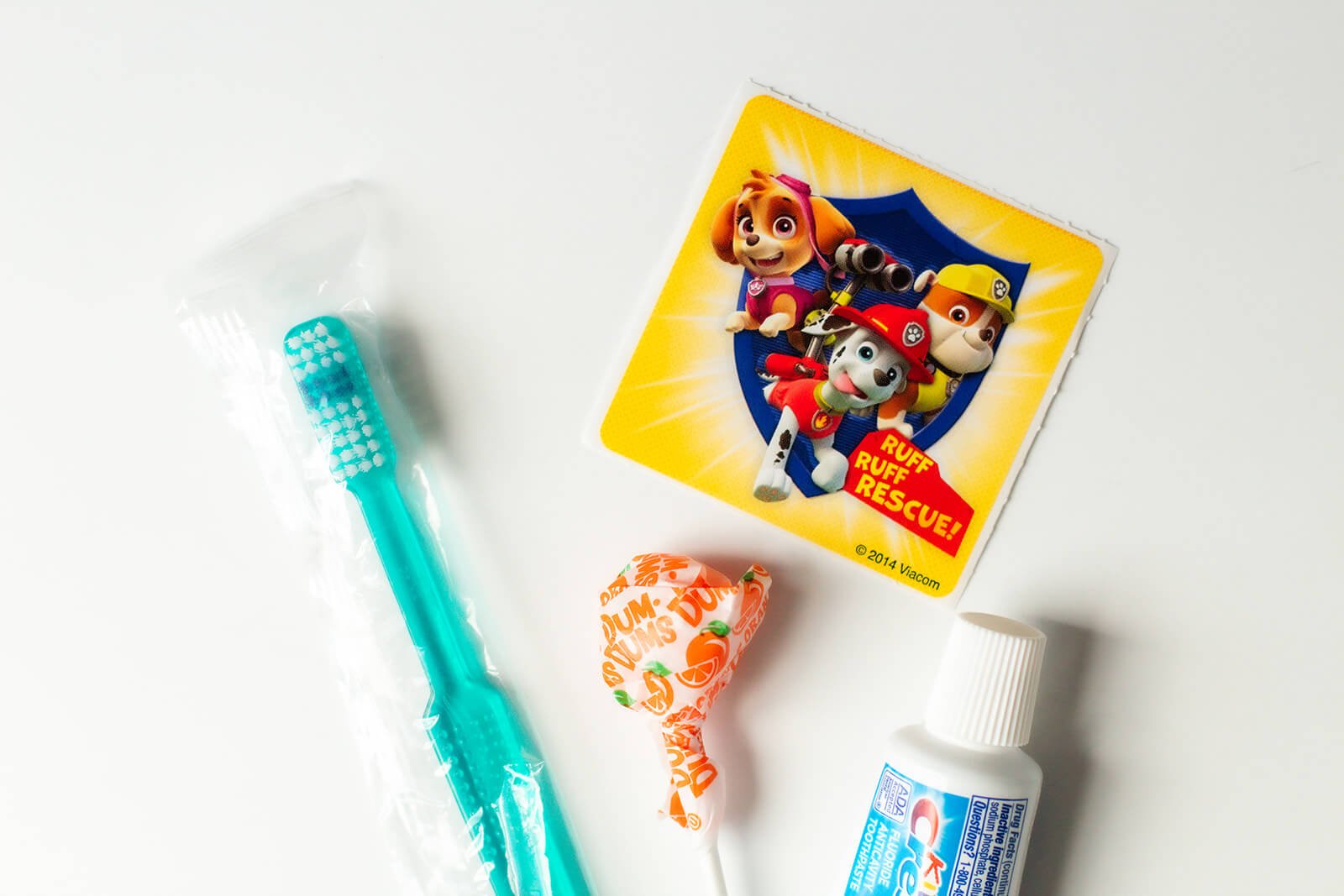 Toothbrush, toothpaste, lollipop and sticker on white table